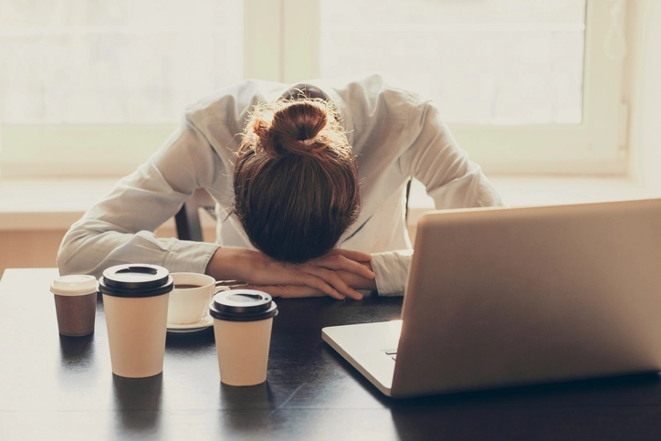 An exhausted woman sleeps at her desk at work